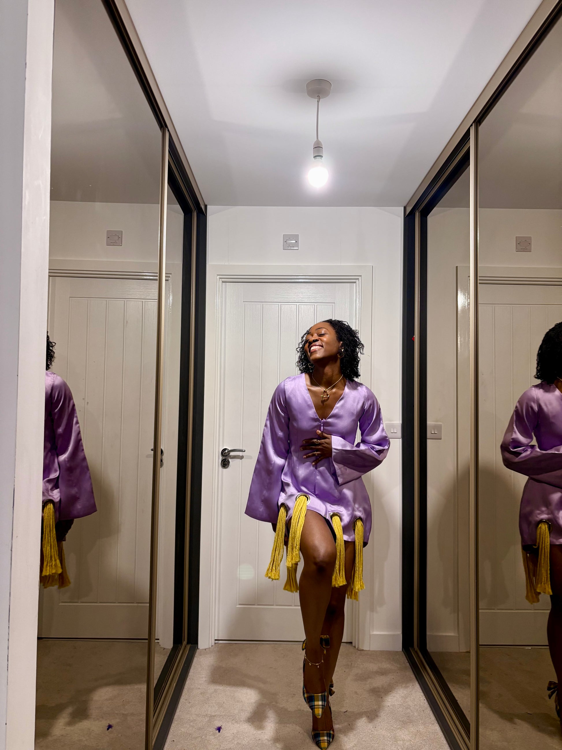 Woman in a purple dress with yellow fringe accents standing in a hallway.